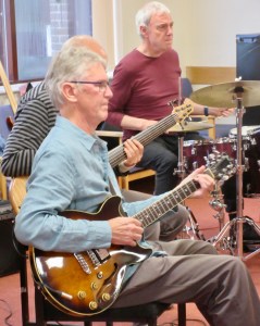People playing guitar, bass guitar and drums in a performance at Grafham